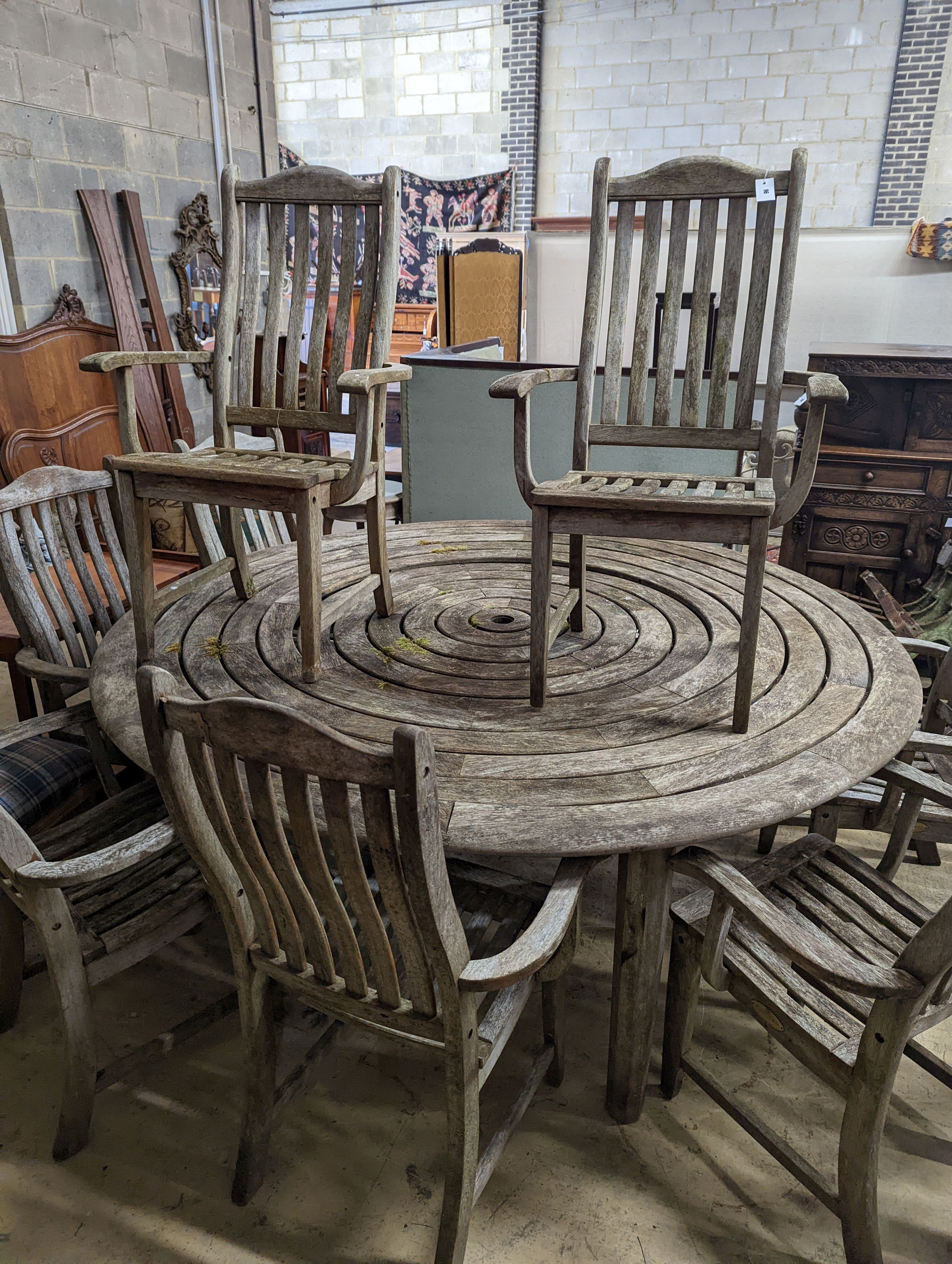 An Alexander Rose weathered teak circular garden table, diameter 190cm, height 74cm and eight elbow chairs